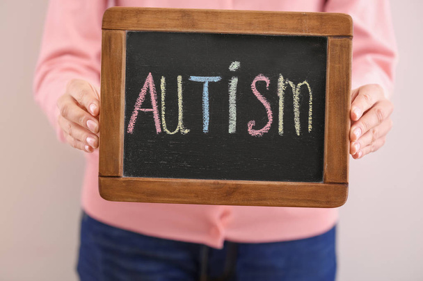 Woman holding chalkboard with word "Autism" on light background - Foto, Imagem