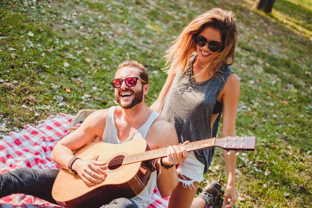 Pari pitää hauskaa kitaran kanssa piknikillä
 - Valokuva, kuva