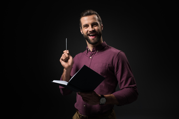 portrait of excited businessman with notebook isolated on black - Photo, Image