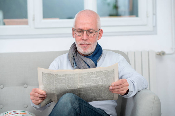 ソファーで新聞を読んでハンサムな中年の男性 - 写真・画像