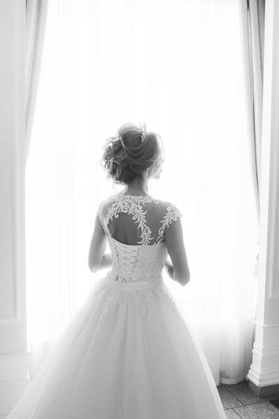 beautiful bride in a wedding dress in a luxurious white room with a large chandelier - Photo, image