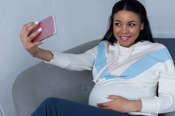 sonriente africano americano embarazada mujer tomando selfie en smartphone
 - Foto, imagen