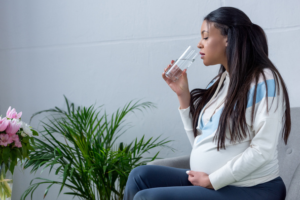 donna africana americana incinta che beve acqua seduta in poltrona
 - Foto, immagini