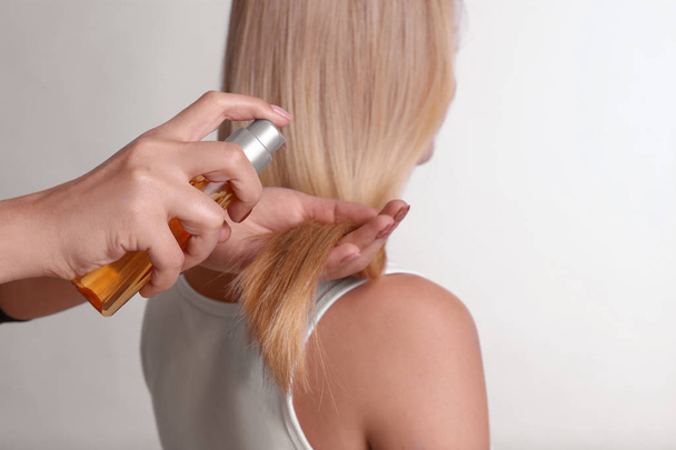Stylist applying oil onto woman's hair on light background - Foto, Imagen