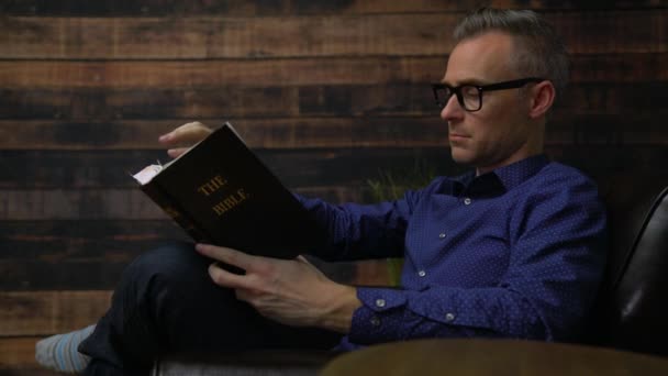 Man in chair reads Holy Bible - Footage, Video