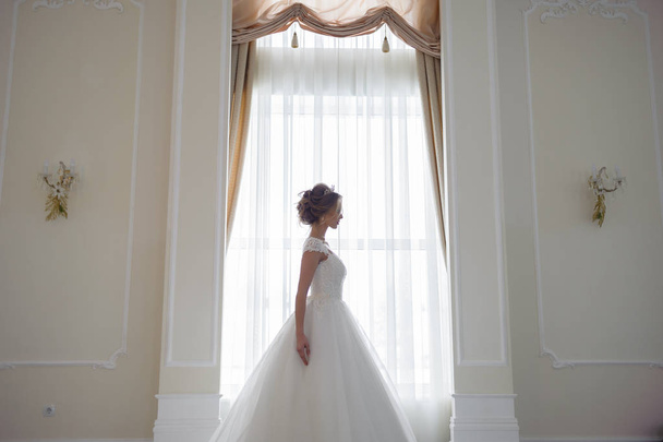 hermosa novia en un vestido de novia en una lujosa habitación blanca con una gran lámpara de araña
 - Foto, Imagen