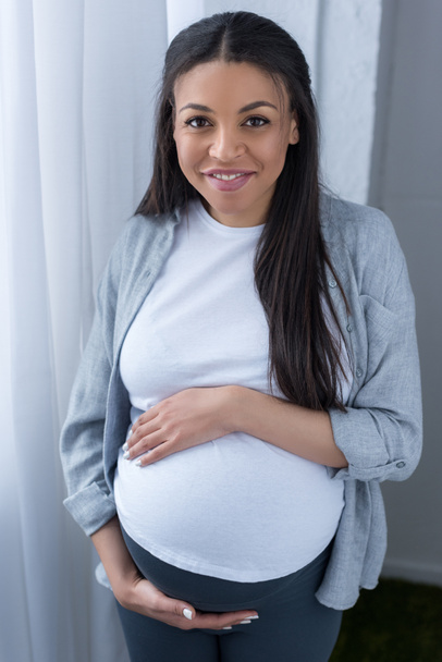 cheerful african american pregnant woman standing at window - Foto, Imagen