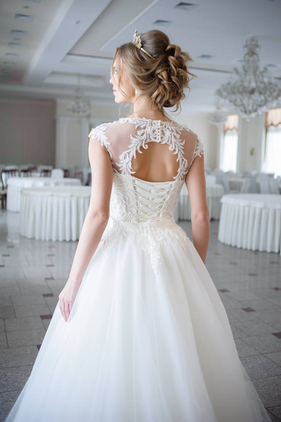krásná nevěsta ve svatebních šatech v luxusní bílé místnosti velký lustr - Fotografie, Obrázek