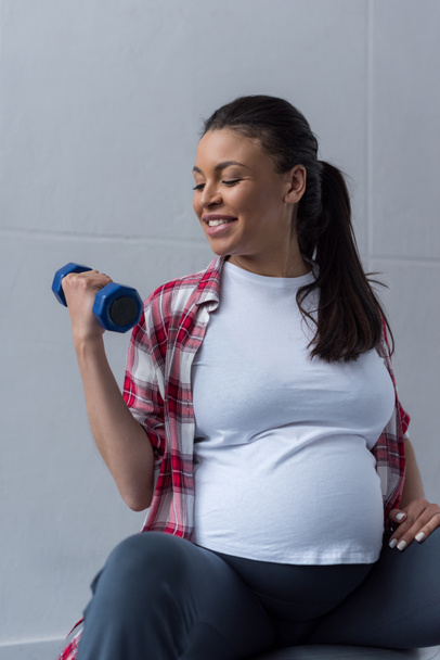 happy african american pregnant woman exercising with dumbbell - Zdjęcie, obraz