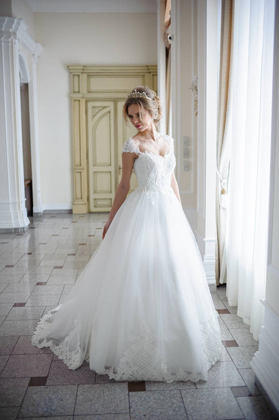 beautiful bride in a wedding dress in a luxurious white room with a large chandelier - 写真・画像