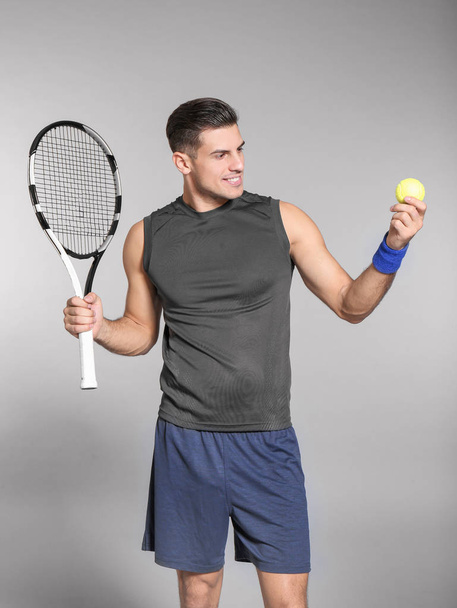 Portrait of handsome man playing tennis against grey background - Фото, зображення