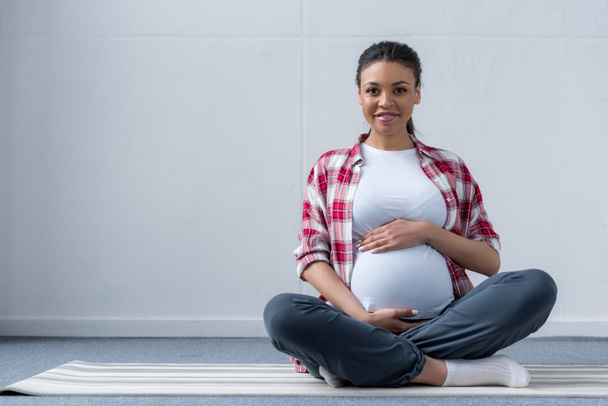 mujer embarazada afroamericana sentada en esterilla de yoga
 - Foto, Imagen