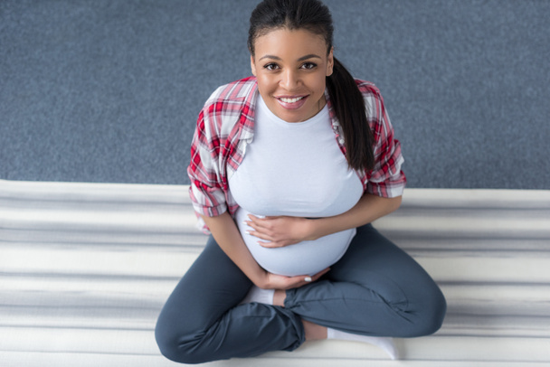 Εναέρια άποψη του χαμογελώντας αφρικανική αμερικανική γυναίκα έγκυος την πρακτική της γιόγκα σε χαλί - Φωτογραφία, εικόνα