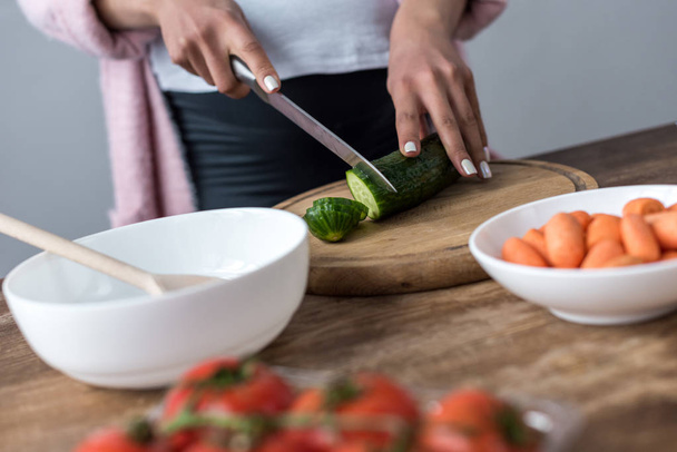 cropped view of woman cutting cucumber and making salad at kitchen - Foto, afbeelding
