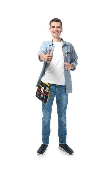 Young plumber with tool belt and wrench on white background - Foto, imagen