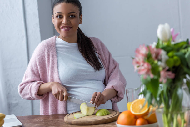 africano americano embarazada mujer cortar manzana en cocina
 - Foto, Imagen