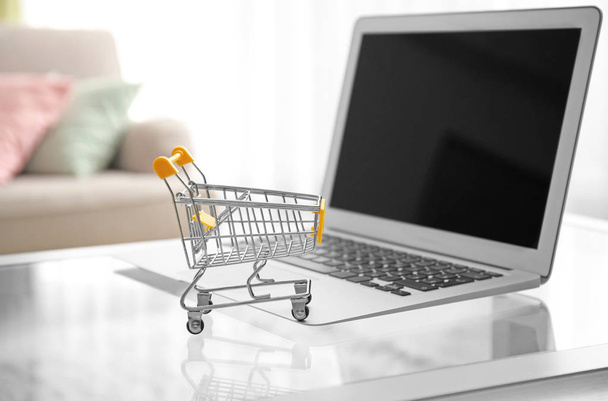 Laptop and small shopping cart on table. Internet shopping concept - Photo, Image