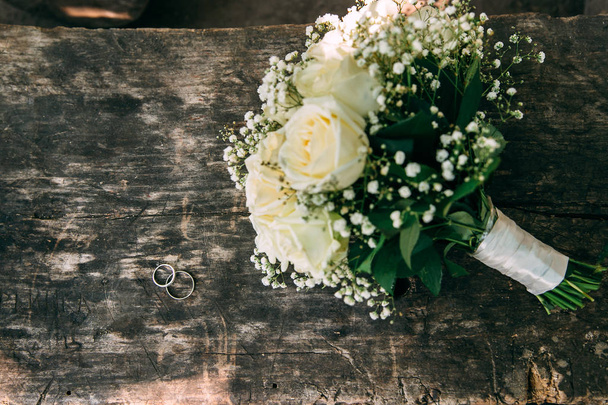 Wedding bouquet of cream roses lies on a wooden surface. Wedding rings - Foto, Imagem
