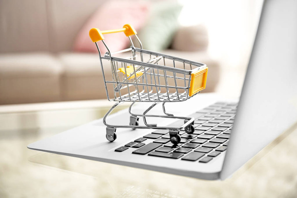 Laptop and small shopping cart on table. Internet shopping concept - Photo, Image