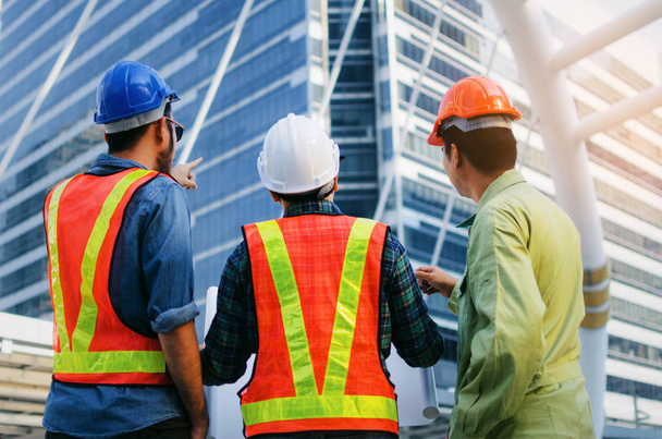 back view group of engineer, technician and architect with safety helmet planning about building plan with blueprint in modern city building background, construction site, industry and worker concept - Photo, Image
