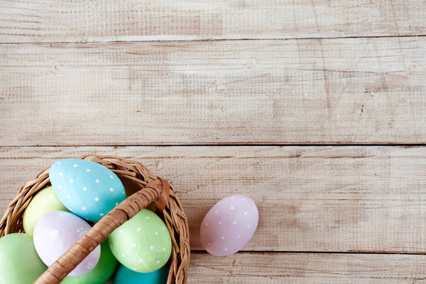 Красочные пасхальные яйца в корзине на деревянном фоне. Пасхальный праздник. Пространство для текста
.  - Фото, изображение