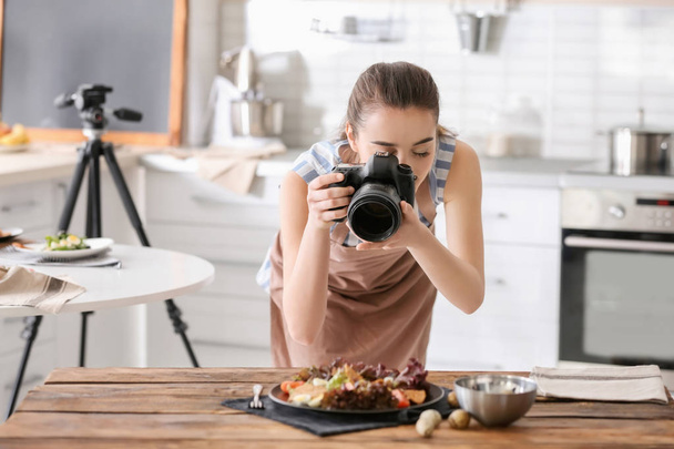 Mujer joven con cámara profesional tomando fotos de naturaleza muerta en la cocina
 - Foto, imagen