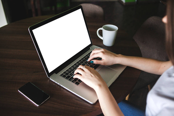 Imagem Mockup de mulher de negócios usando e digitando no laptop com tela branca em branco e xícara de café na mesa no moderno café loft
 - Foto, Imagem