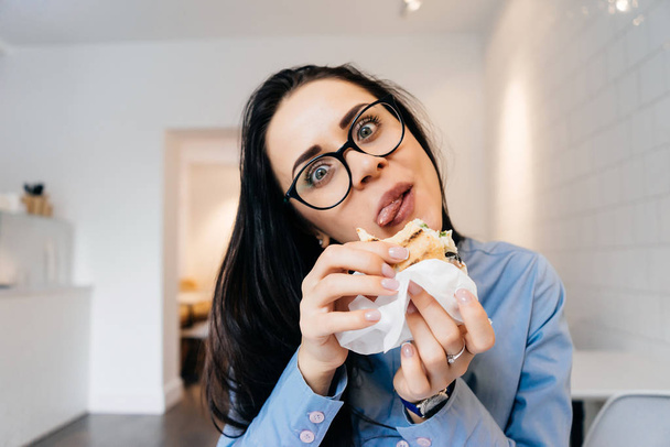 woman sitting at the office at the table and eating a sandwich - Фото, изображение