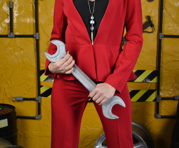 Fashionable mechanic girl in trendy clothes is holding a wrench on the background of the workshop of an auto mechanic. Fashion shooting, an unusual image. Lifestyle. - Foto, Imagen