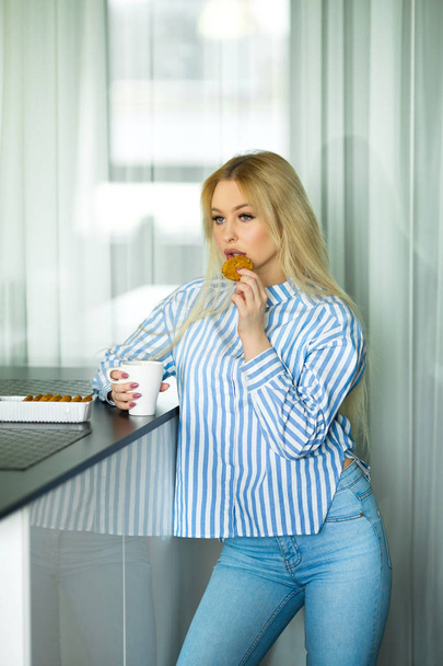 beautiful young blonde girl at home in the kitchen drinking coffee at breakfast - Фото, зображення