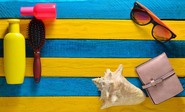 Copia el espacio de accesorios de moda para relajarse en la playa y la belleza en una mesa de madera azul amarillo. Monedero, frasco de perfume, peine, gafas de sol, concha, espejo, bloqueador solar
. - Foto, imagen