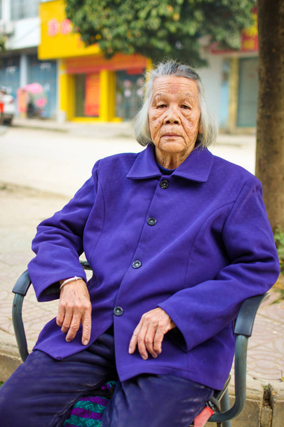 Vezető ázsiai nő ül egy széken, ház előtt - Fotó, kép