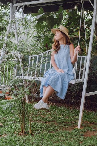 Young woman in a hat sits on a white swing - Foto, Imagem