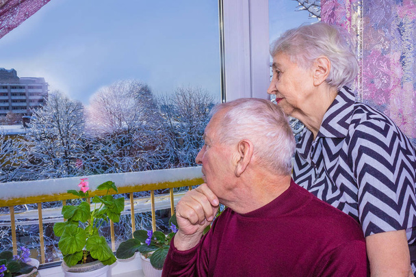 O triste casal sênior em casa sentado perto da janela juntos
 - Foto, Imagem