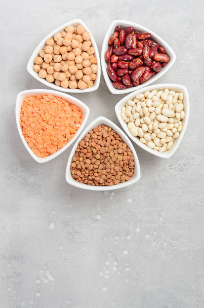 Selection of dry legumes, lentils and peas in white bowls on gray concrete background. Top view, flat lay, copy space. - Fotoğraf, Görsel