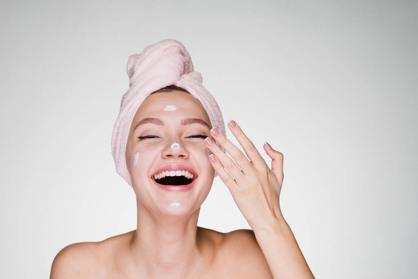 happy woman with a towel on her head puts on a face cream - Φωτογραφία, εικόνα