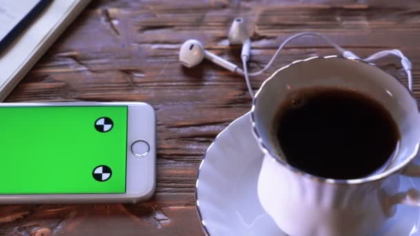 Coffee cup next to the mobile device both on a wooden table. Studio shot. - Materiaali, video