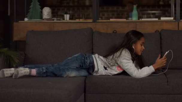 Χαριτωμένο αφρικανική αμερικανική κορίτσι ακούγοντας μουσική στον καναπέ - Πλάνα, βίντεο