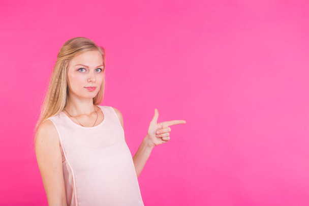Jonge vrouw wijzend op roze achtergrond met kopie ruimte - Foto, afbeelding