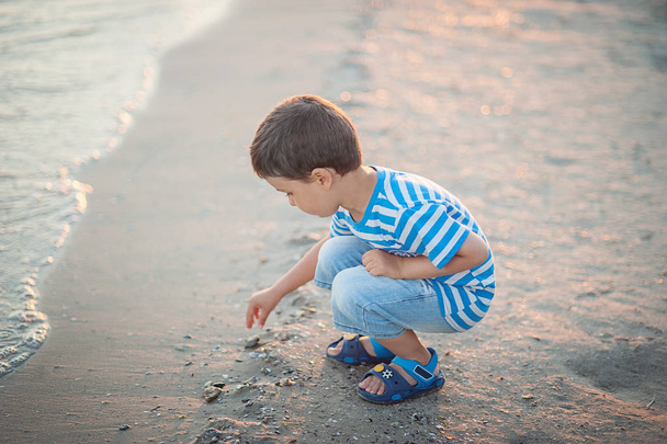little boy by the sea throws stones in water at sunset. Happy childhood. - Zdjęcie, obraz