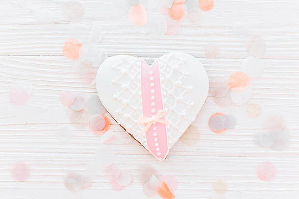 pink cookie heart on white rustic wooden background with confetti flat lay in soft light. happy valentine's day. happy mother's women's day greeting card. space for text - Photo, Image