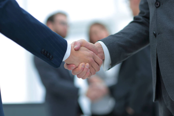 Two businessmen shaking hands with colleagues  on background. - Foto, imagen