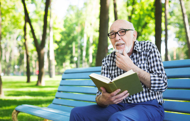 Elderly man in casual reading outdoors - Фото, изображение