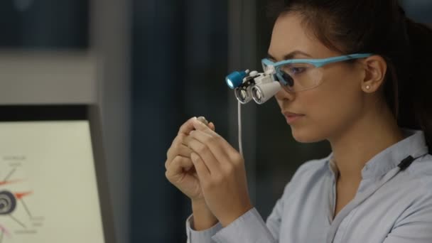 4K Audiology doctor wearing magnifying glasses and looking at a hearing aid - Filmmaterial, Video