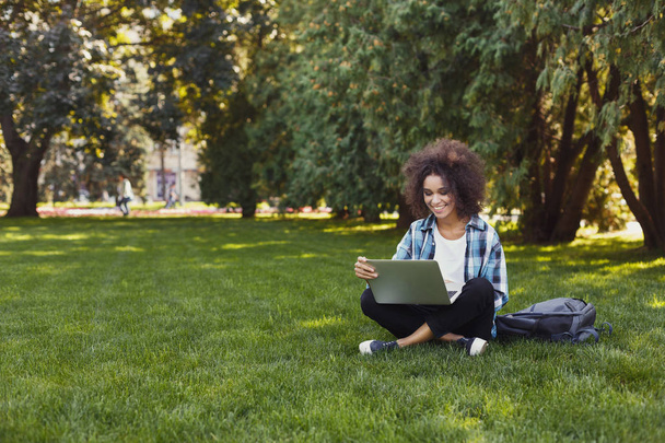 Cheerful young woman using laptop in park - Photo, image
