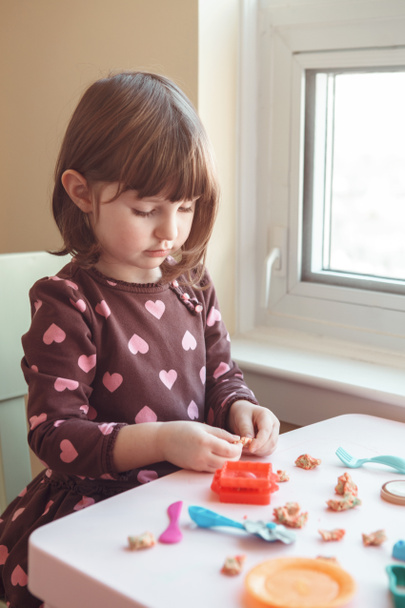 Aranyos fehér kaukázusi óvodás lány játék gyurma playdough beltéri otthon portréja. Korai kreativitás agy fejlődés fogalmát. A gyermekek tevékenységét. Finom motoros készségek. - Fotó, kép