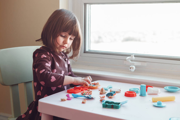 Portret ładny biały Kaukaska przedszkolak dziewczyna bawi plastelina playdough pomieszczeniu w domu. Koncepcja rozwoju mózgu początku kreatywności. Aktywność dzieci. Zdolności motoryczne. - Zdjęcie, obraz