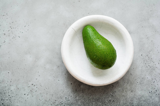 Fresh raw avocado in white old ceramic plate on gray concrete background. Selective focus. Top view. - Photo, image