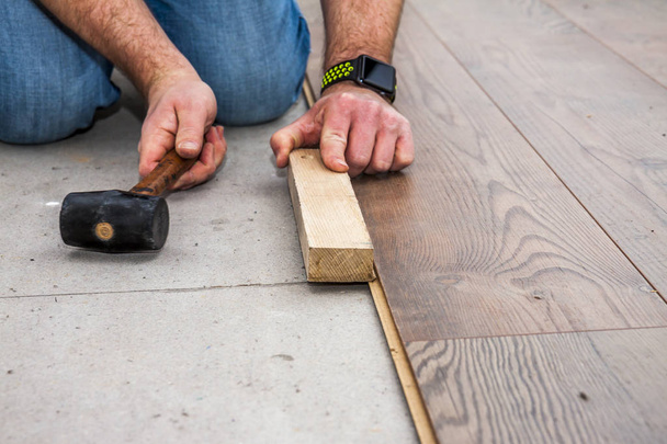 Homem que estabelece laminado usando martelo e bloco de madeira
 - Foto, Imagem
