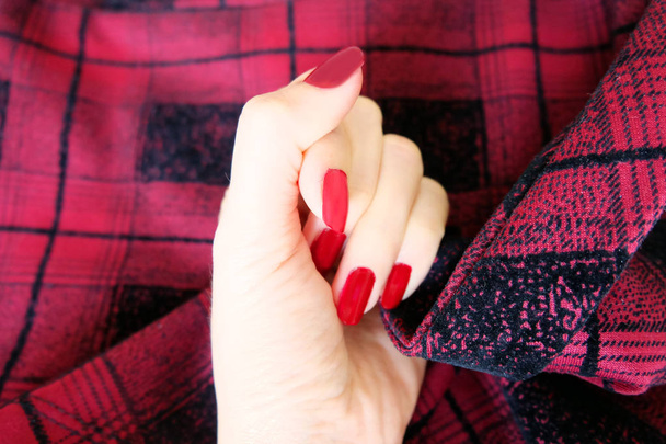 Schönheit rote Maniküre Nagel mit Gellack. Frau Hand mit roten Nägeln auf dem roten scot Stoff Hintergrund ideal für jeden Einsatz. - Foto, Bild